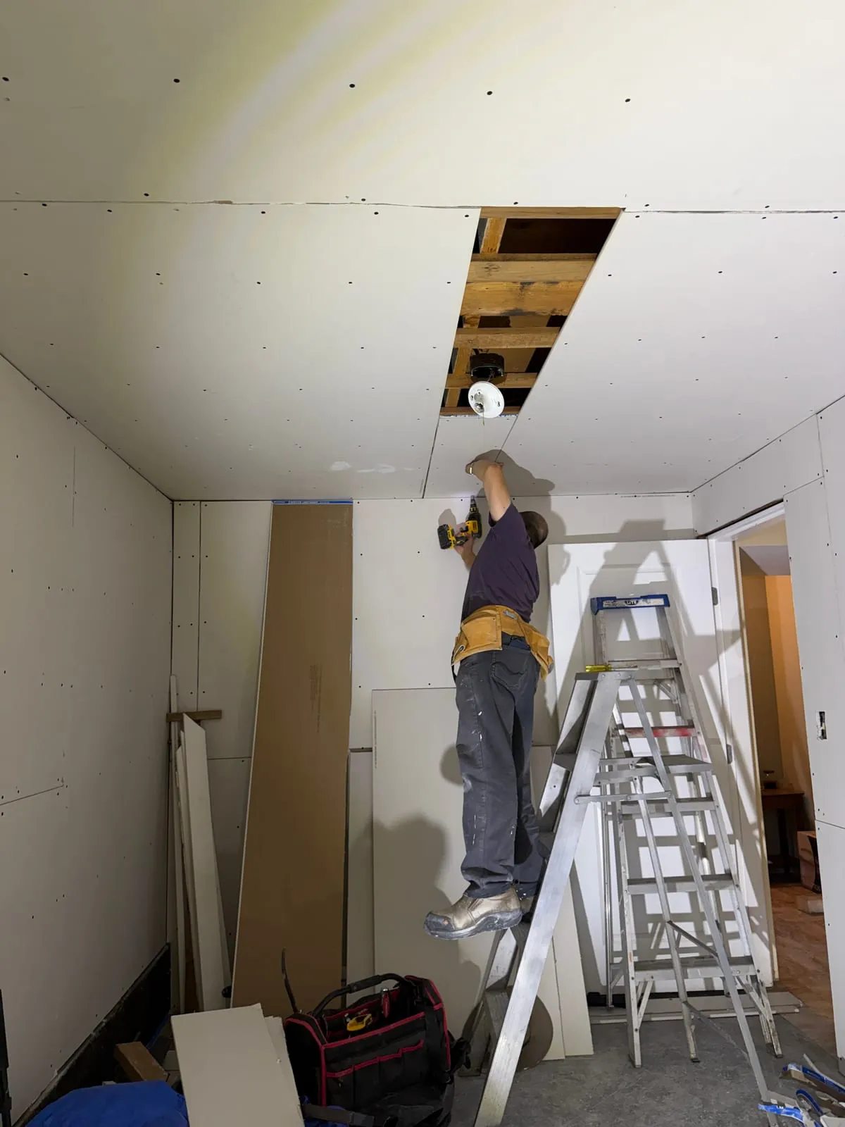 Fastening a ceiling drywall strip around the light opening.