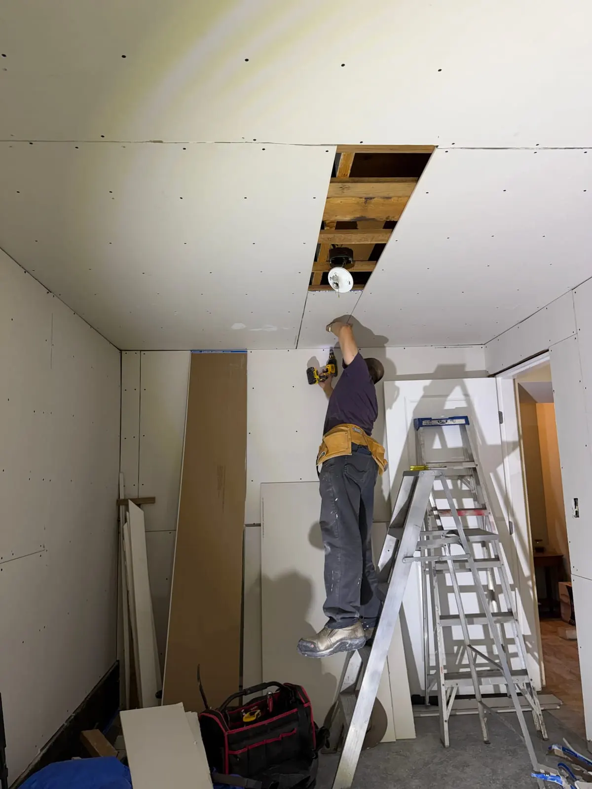 Fastening a ceiling drywall strip around the light opening.